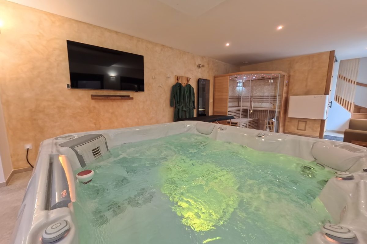 Jacuzzi éclairé au premier plan, baie vitrée donnant sur la terrasse