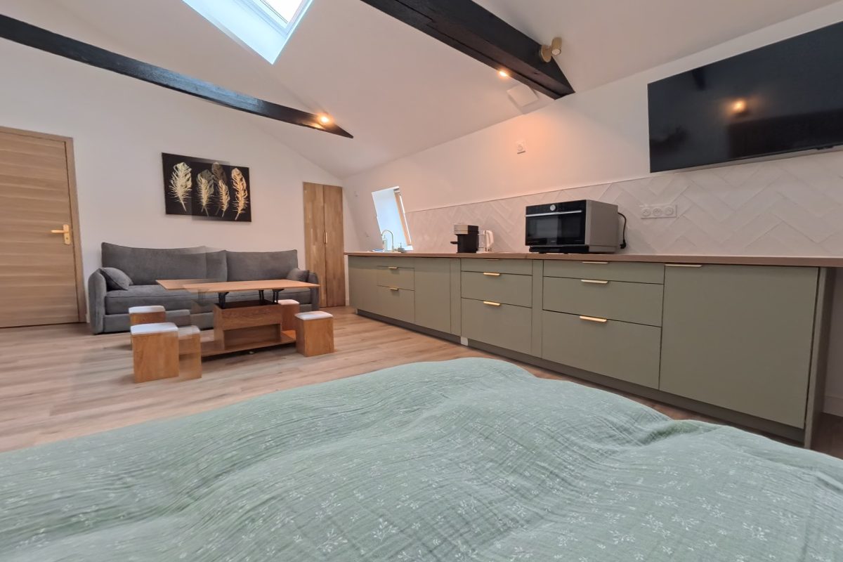 Lit double au linge vert sauge sous les poutres et le velux