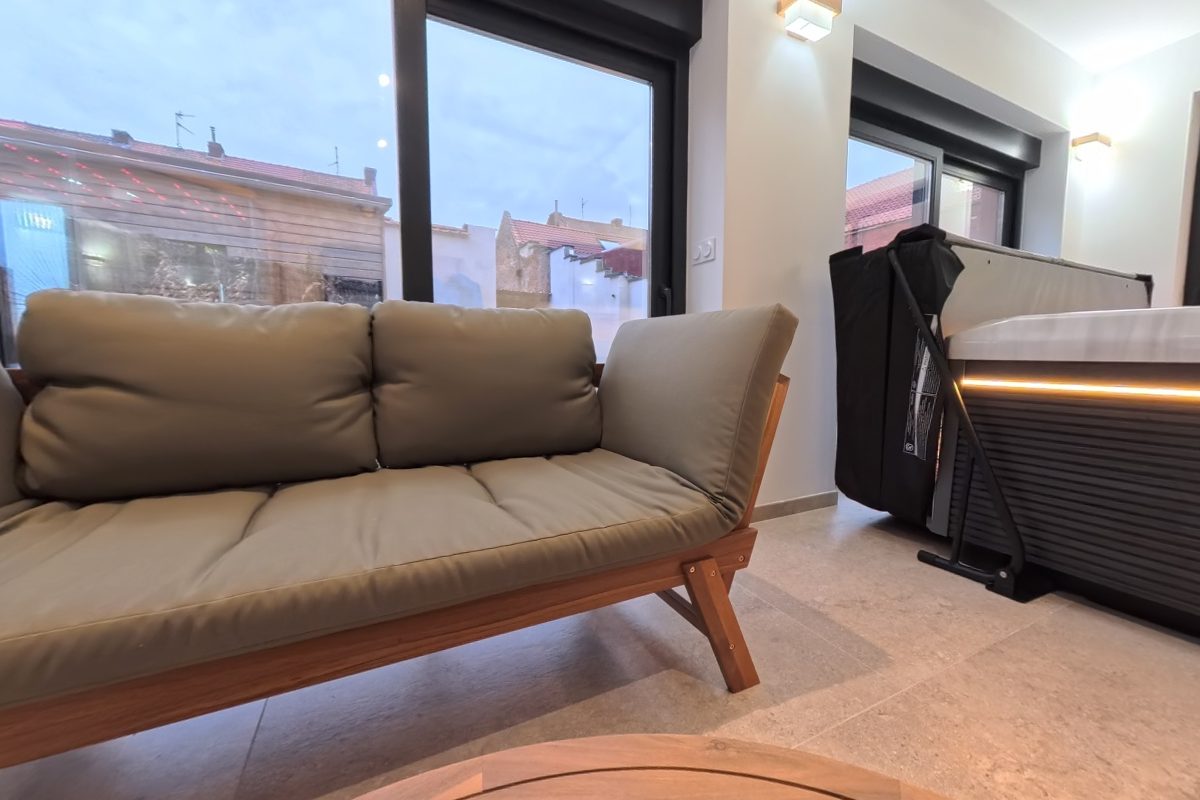 Salon du spa avec banquette verte, jacuzzi éclairé et sauna vitré